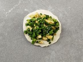 取小份面团，用擀面杖擀成四边薄，中间厚的面片，放上馅料