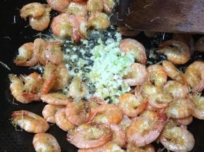炒至大虾表皮焦黄，下入蒜末和葱白，转小火煸出香味。