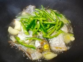 两面煎至金黄后，放入姜片、蒜片、青椒丝