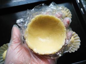 隔保鲜膜将挞皮铺在模具上，粘合紧，高出模具少许