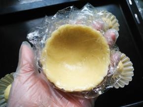 隔保鲜膜将挞皮铺在模具上，粘合紧，高出模具少许