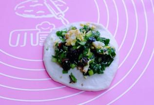 取一小块面团用擀面杖擀圆饼，包上拌好的馅儿。