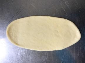 醒面结束，取一个面团擀成牛舌状。翻面，光滑面朝下。