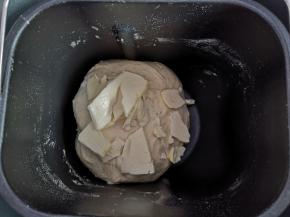 5、面团变得光滑，能拉出膜时，加入切成小块的黄油，继续揉面。面团会越来越光滑，拉出的薄膜变得结实时，将面团取出。