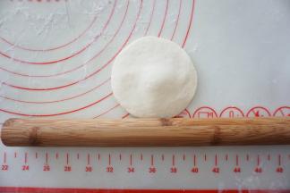 取一个面团，按扁，擀成中间厚四周薄的圆片。