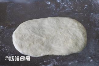 取一个醒发后的面团，拍扁翻面擀开长长圆形。