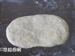 取一个醒发后的面团，拍扁翻面擀开长长圆形。