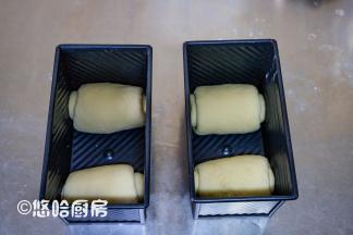 醒发后的面团擀开，从上往下卷起，捏紧收口，2个面团分别放在吐司盒的2端，吐司盒放入烤箱中，下面放一碗热水，进行二次发酵。