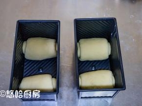 醒发后的面团擀开，从上往下卷起，捏紧收口，2个面团分别放在吐司盒的2端，吐司盒放入烤箱中，下面放一碗热水，进行二次发酵。