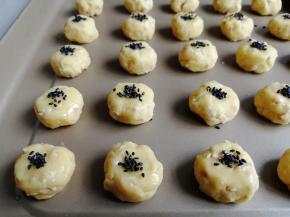 再将圆圆的小面团稍微压扁一下，在表面刷上全蛋液，再粘上黑芝麻