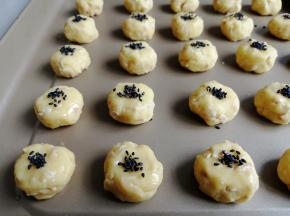 再将圆圆的小面团稍微压扁一下，在表面刷上全蛋液，再粘上黑芝麻