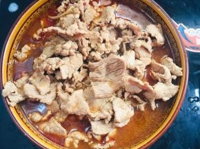 把煮好的肉片倒进碗里的配菜上。