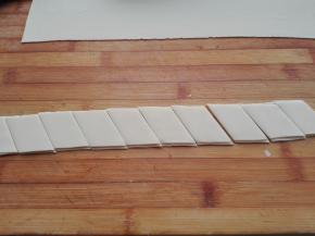 将其切好的长条面片，分别在其上面撒上点干粉，摞在一起，斜着切成菱形。