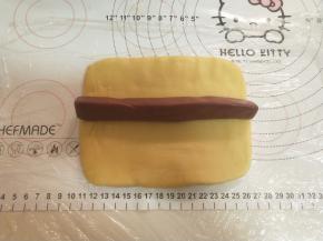 将黄色面团擀成15厘米长的长方形。将60克的红面团搓成条放在黄面团中间。卷起来。