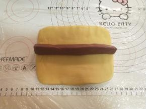 将黄色面团擀成15厘米长的长方形。将60克的红面团搓成条放在黄面团中间。卷起来。