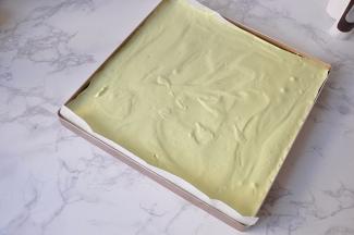 将拌好的蛋糊从高处倒入铺了油纸的烤盘中。