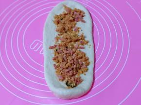 取一块面团，用擀面杖擀开，将气泡拍破，再放入肉松馅，撒上白芝麻。(留一点肉松和芝麻，撒发酵好的面包胚上面)