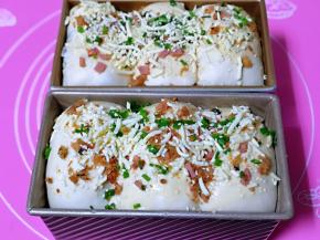 放入烤箱进行发酵，放入一杯开水，保持面包胚的湿度，发酵至9分满，取出刷上蛋液，撒上马苏里拉芝士，肉松，白芝麻，葱花。