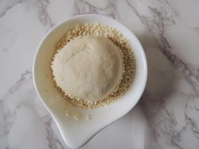 轻轻拿起一个面团，翻转过来放入装有白芝麻的深碟中，让面团表面粘满白芝麻。