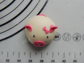 将做好的猪鼻子、猪耳朵、猪尾巴和蝴蝶节底部蘸一点清水，摆放到白色面团的对应位置。黑芝麻蘸水沾到面团上，当做眼睛。