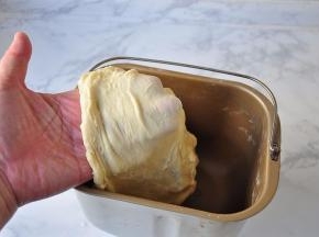 启动面包机的揉面程序，15分钟后面团表面光滑柔软，轻拉可见薄膜，这时就可以加入黄油了。