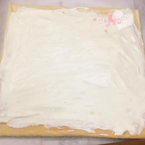 晾凉翻面，揭去油布。带花纹的那面盖上油纸，翻面，切去尾端，抹上淡奶油。