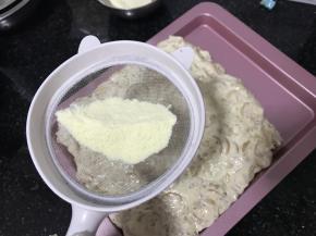 不粘烤盘中先撒一层奶粉，把做好的雪花酥放入盘中压实，压实后撒一层奶粉