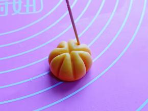取一小块面团，揉圆，用牙签做出南瓜的形状即可。(首先牙签在面团的中间压出十字，之后再如图中所示，将周边压出南瓜的花纹即可)