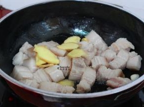 用炒锅，烧热，少许油，把汆烫好的五花肉块放入锅，加几片生姜一起翻炒至微黄，油脂出来。