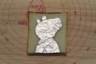 准备一张锡纸，剪成佩琪的轮廓，放在吐司片上。