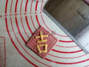 在小猪馒头醒发的时候，紧接着做母猪馒头，红色面团擀平，切成大的正方形，黄色面团搓细长，再压扁一下，切出适当的长度，拼出“吉”字，粘在红色面片上面。用牙签戳出一排小孔，这样大吉字就做好了