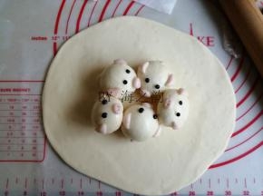 将215克大面团揉片刻排气（因为做好这些步骤，面团已经发酵差不多有两倍大了），再擀成椭圆面皮，中间厚，四周薄一点，面皮不要擀太薄。将每只蒸好晾凉的小猪馒头刷一层玉米油，防粘，摆在面皮中间部位