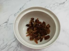 把葡萄干儿洗干净，挤干水分，放入碗中