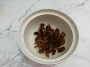 把葡萄干儿洗干净，挤干水分，放入碗中