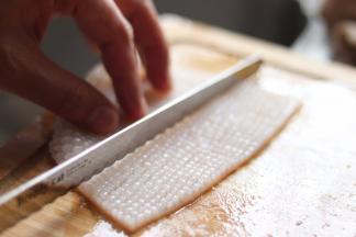 墨鱼切花，从墨鱼的内部切十字，不要切断，形成小块，根据虾的大小，切出长条，用于裹虾。