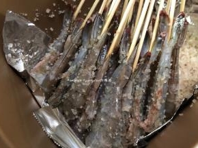 把混合好的一半海盐倒入面包机桶中，然后把串好的虾也摆入面包机中，如果竹有点长可以剪短点，这样子后面面包机的盖子才可以盖得上