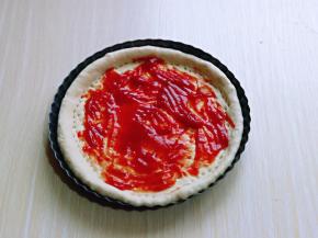 取一块面团擀成与披萨盘一样大的披萨皮，再用叉出洞洞，涂抹上番茄酱。