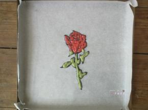 在绘有玫瑰花的油纸反面根据线条勾勒出玫瑰花的形状，先用黑色面糊描边，再用红色面糊和绿色面糊分别填充花瓣部分和茎叶部分，画好后立即送入预热好的烤箱烘烤1分钟定型