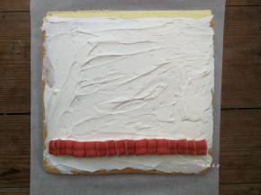 将晾凉的蛋糕片放在干净的油纸上，没有彩绘玫瑰的那面朝上，四周切平整，底端45度斜切，然后抹上打发的淡奶油，铺上一排夹心用的心型红丝绒蛋糕，铺夹心的时候要挨着铺紧凑些，不能留有空隙