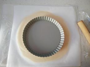 取出面团上面铺一层油纸，用擀面杖先按压几次，再慢慢擀开，将面团擀的与模具大一圈。