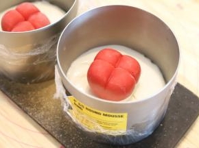 开始组装爱巢蛋糕：冰箱中取出慕斯圈，倒入一点酸奶慕斯液，将两个爱心草莓慕斯放在中间。