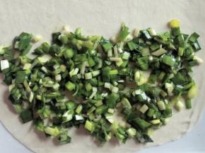 把适量韭菜馅摊在一半薄饼上