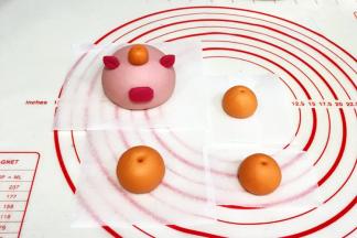 把橙色的面团分出1个3克小剂子搓圆，粘在小猪的脑袋上，其余的面团随意分成3份滚圆，用尖的筷子或竹签在圆面团上扎个孔。