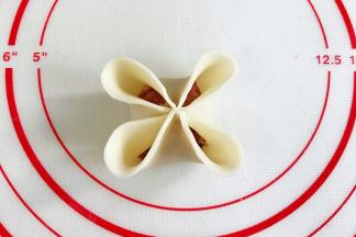 先给饺子皮对角刷点水，筷子对角夹紧，再把每一个花瓣边缘捏薄些。