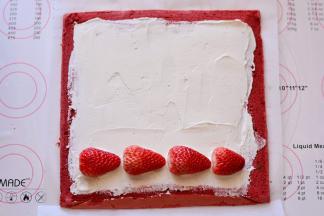 把晾凉的蛋糕卷放在一张油纸上，抹上打发好的淡奶油，摆放上草莓，再抹一屋奶油，把草莓包裹起来