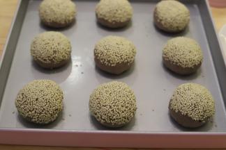 再次将面团排气整圆，表面喷少许的清水，粘上熟白芝麻，放入烤盘。