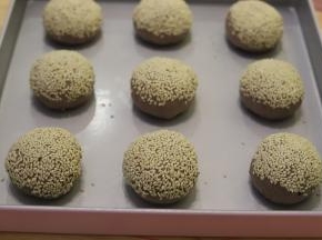 再次将面团排气整圆，表面喷少许的清水，粘上熟白芝麻，放入烤盘。