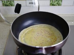 因为面糊里有加入了玉米油，这样子在烙饼的时候就不用再刷油了，用汤勺盛一勺面粉在锅里，然后摊均开。