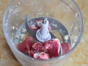 将去掉筋的猪肉块放入绞肉机中，加入葱、蒜。