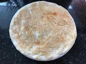 将松弛后的面团擀开摊成圆饼，放入抹了油的烤盘中，面饼的边缘要略高，用叉子或者牙签在面饼上叉些小孔，防止饼皮在烘烤过程中中间凸起